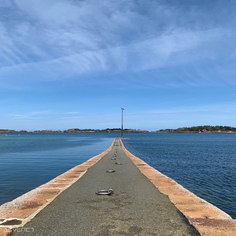 Embarcadère en pierre plongeant dans la mer, avec un lampadaire au bout de la jetée.